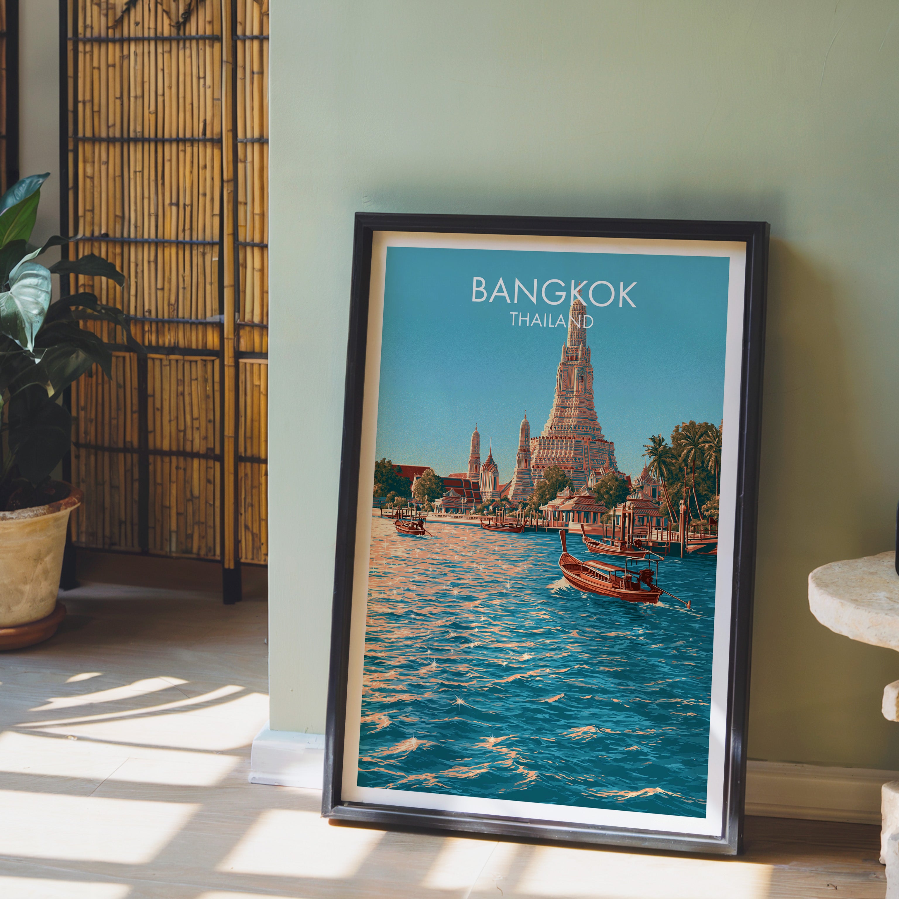 Wat Arun Bangkok Thailand wall art in a black frame leaning against a sage green wall beside a bamboo screen