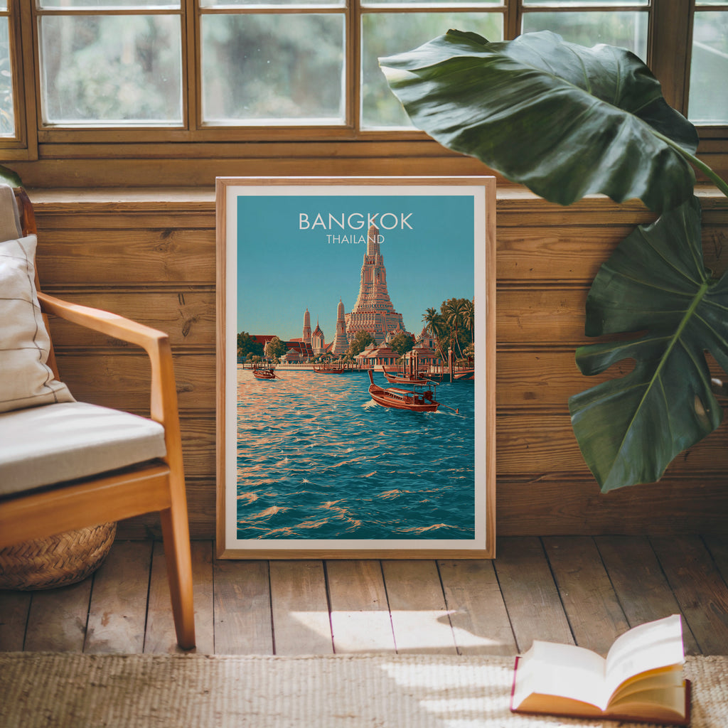 Framed Wat Arun Bangkok Thailand poster leaning against a timber cabin wall with monstera leaves and an open book