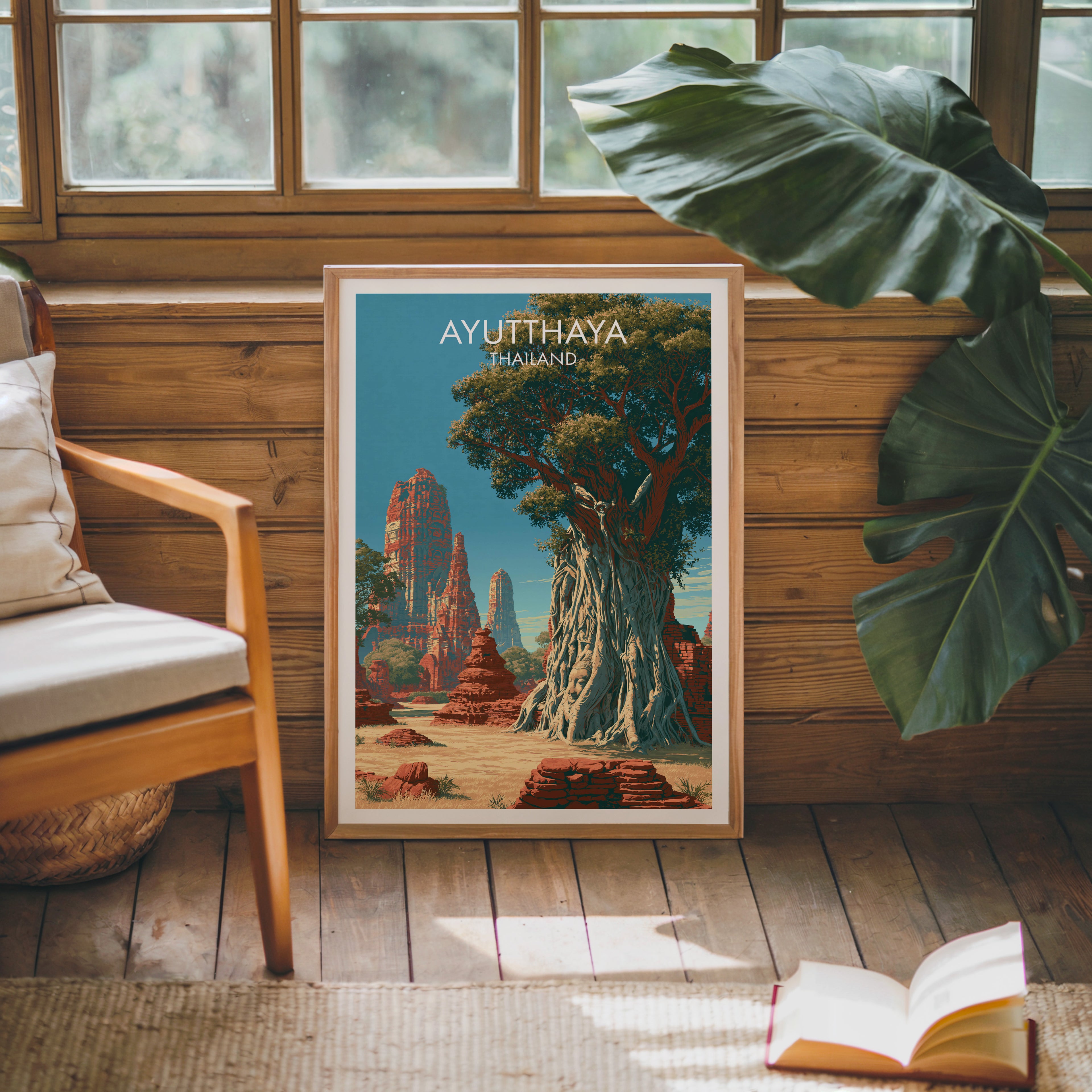 Framed Wat Mahathat Ayutthaya Thailand poster leaning against a timber cabin wall with monstera leaves and an open book