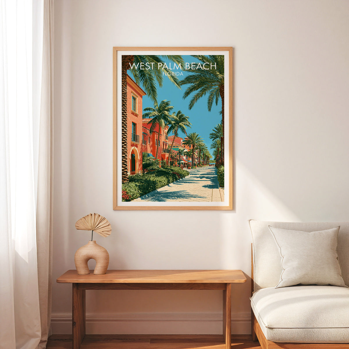 Florida palm street poster in an oak frame above a wood bench, cream armchair, linen curtain and palm fan.