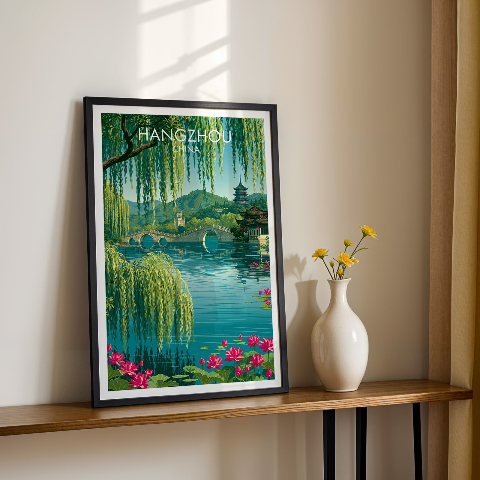 Black framed West Lake Hangzhou China print on a narrow hallway console in sunlight, styled with yellow flowers