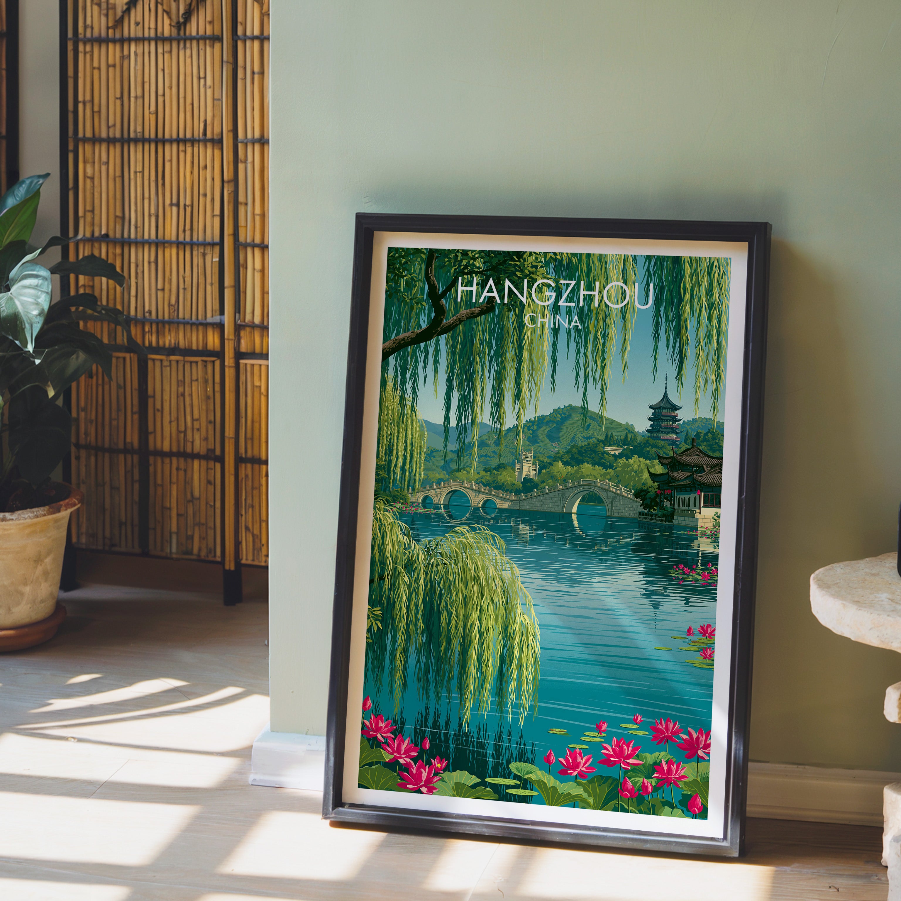 West Lake Hangzhou China wall art in a black frame leaning against a sage green wall beside a bamboo screen