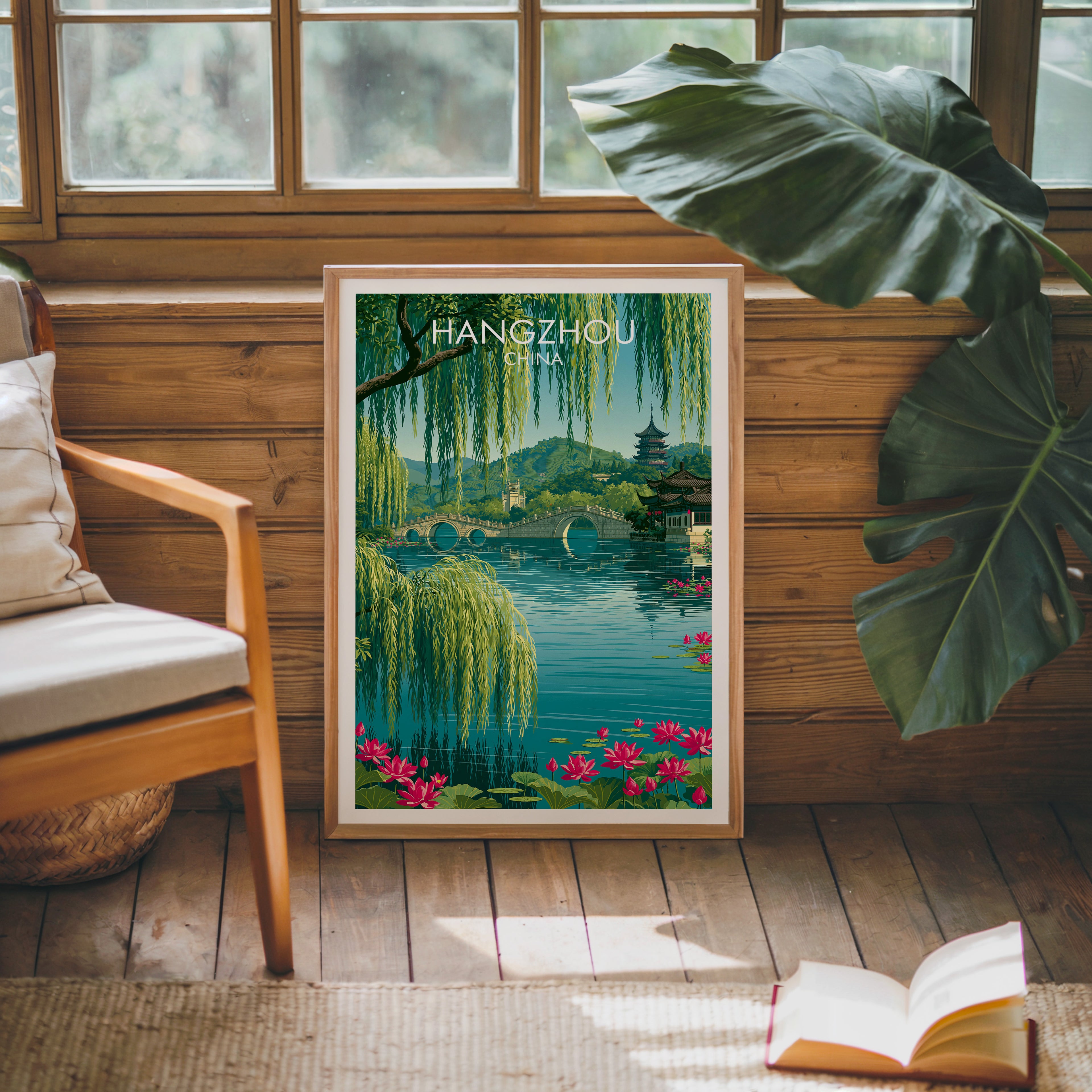 Framed West Lake Hangzhou China poster leaning against a timber cabin wall with monstera leaves and an open book