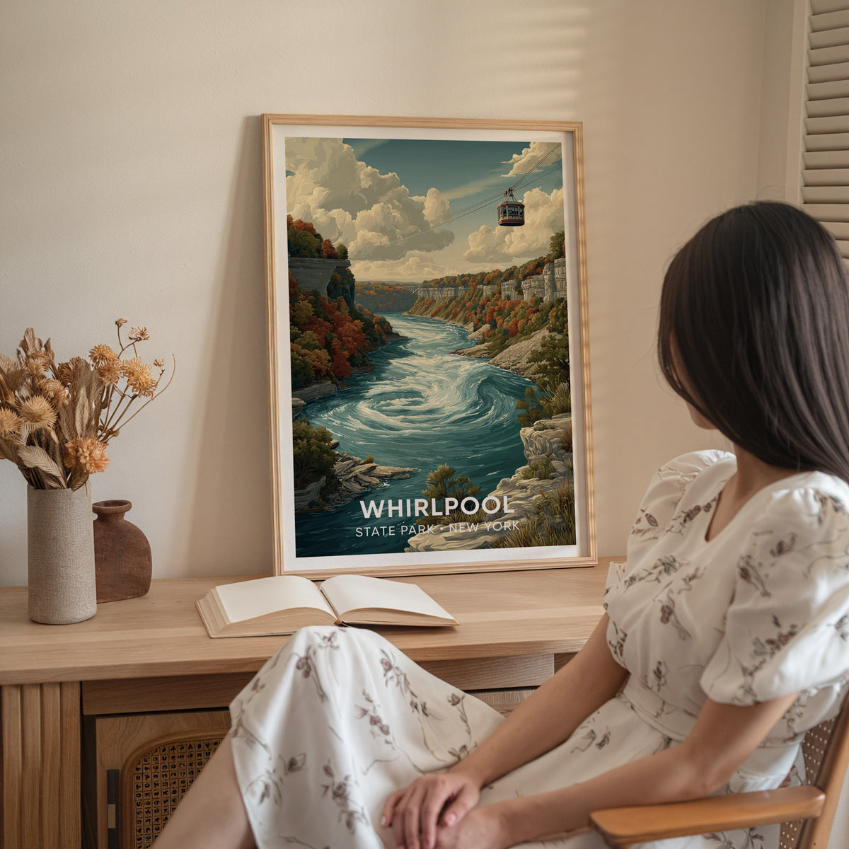 Whirlpool State Park print on a wood sideboard with dried flowers and an open book, a woman seated