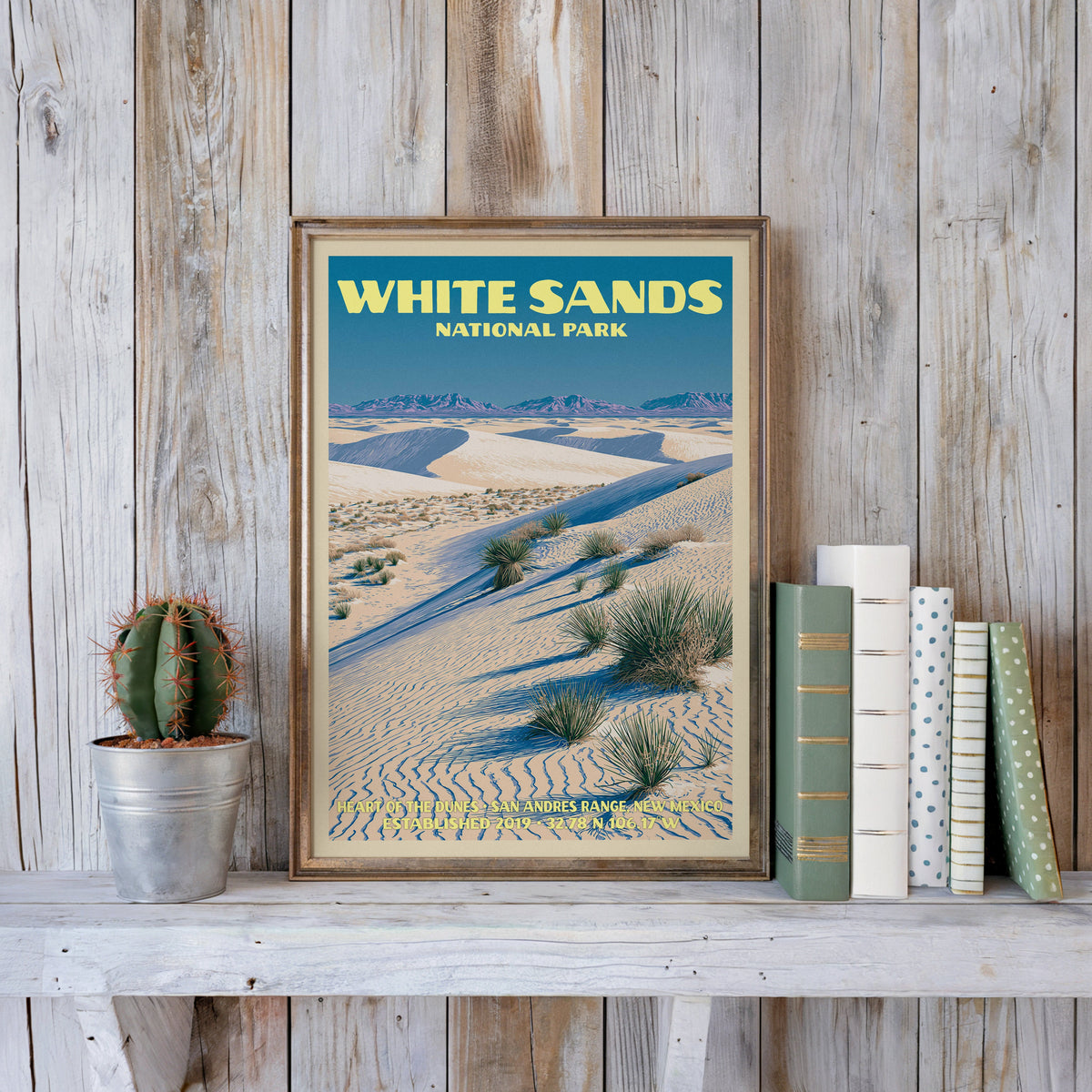 White Sands vintage poster in a slim gold frame on a whitewashed plank wall beside a cactus and pastel books