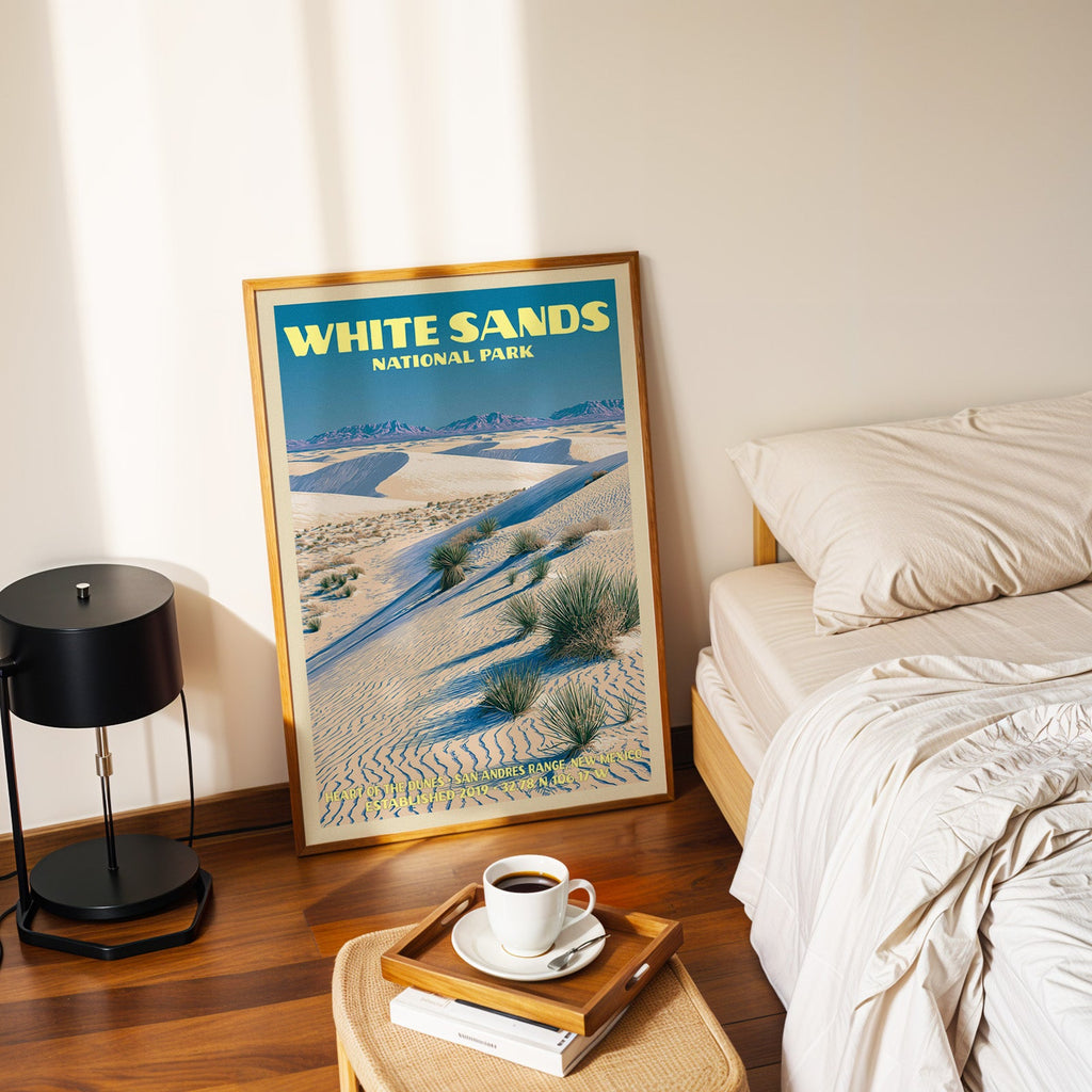 Heart of the Dunes poster in a gold frame on the bedroom floor beside a made bed and a black table lamp