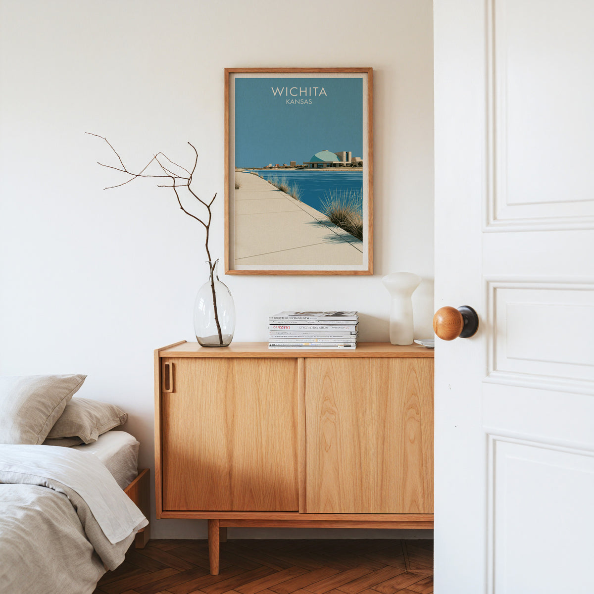 Wichita travel print in an oak frame on a pale sideboard with dried branches and magazines.