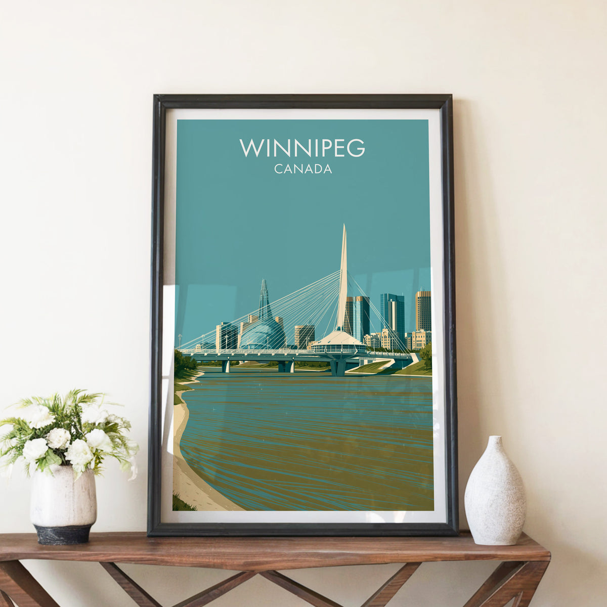 Winnipeg Red River bridge print in a black frame on a walnut console beside white peonies