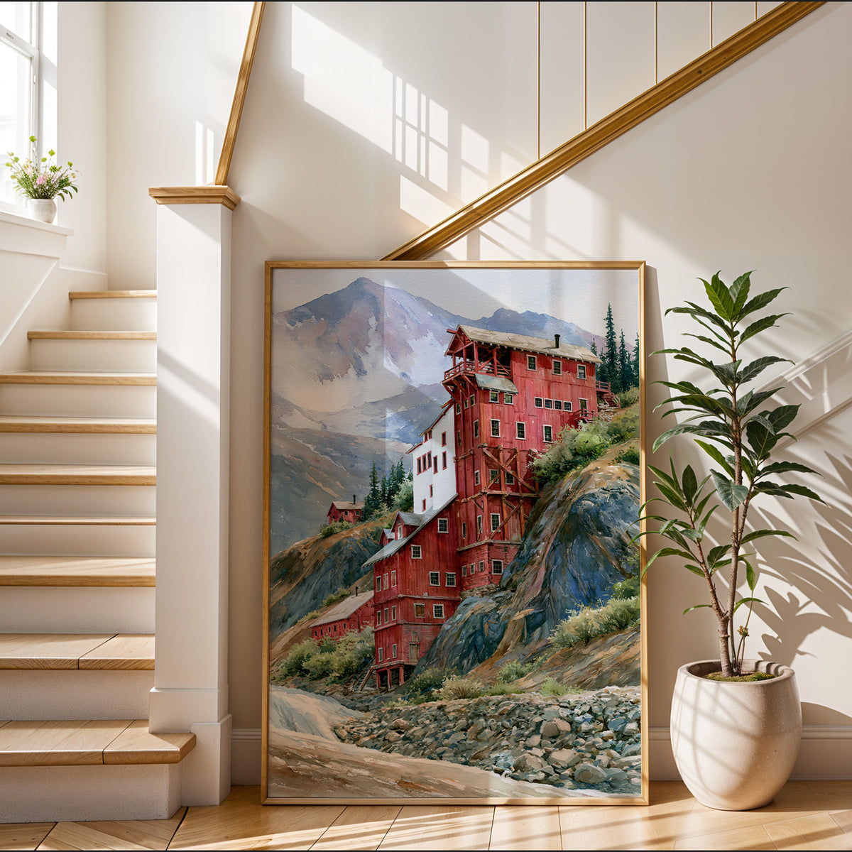 Gold-framed Wrangell-St. Elias watercolor art print leaning in a sunlit entryway beside a staircase