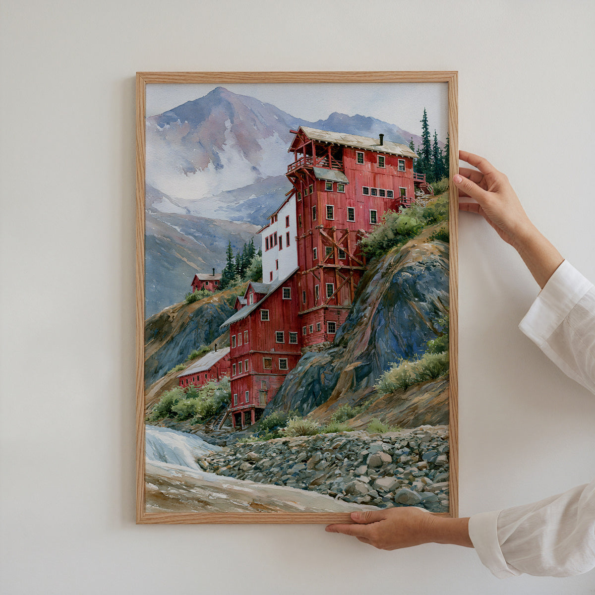 Hands holding an oak-framed Wrangell-St. Elias watercolor art print against a plain white wall