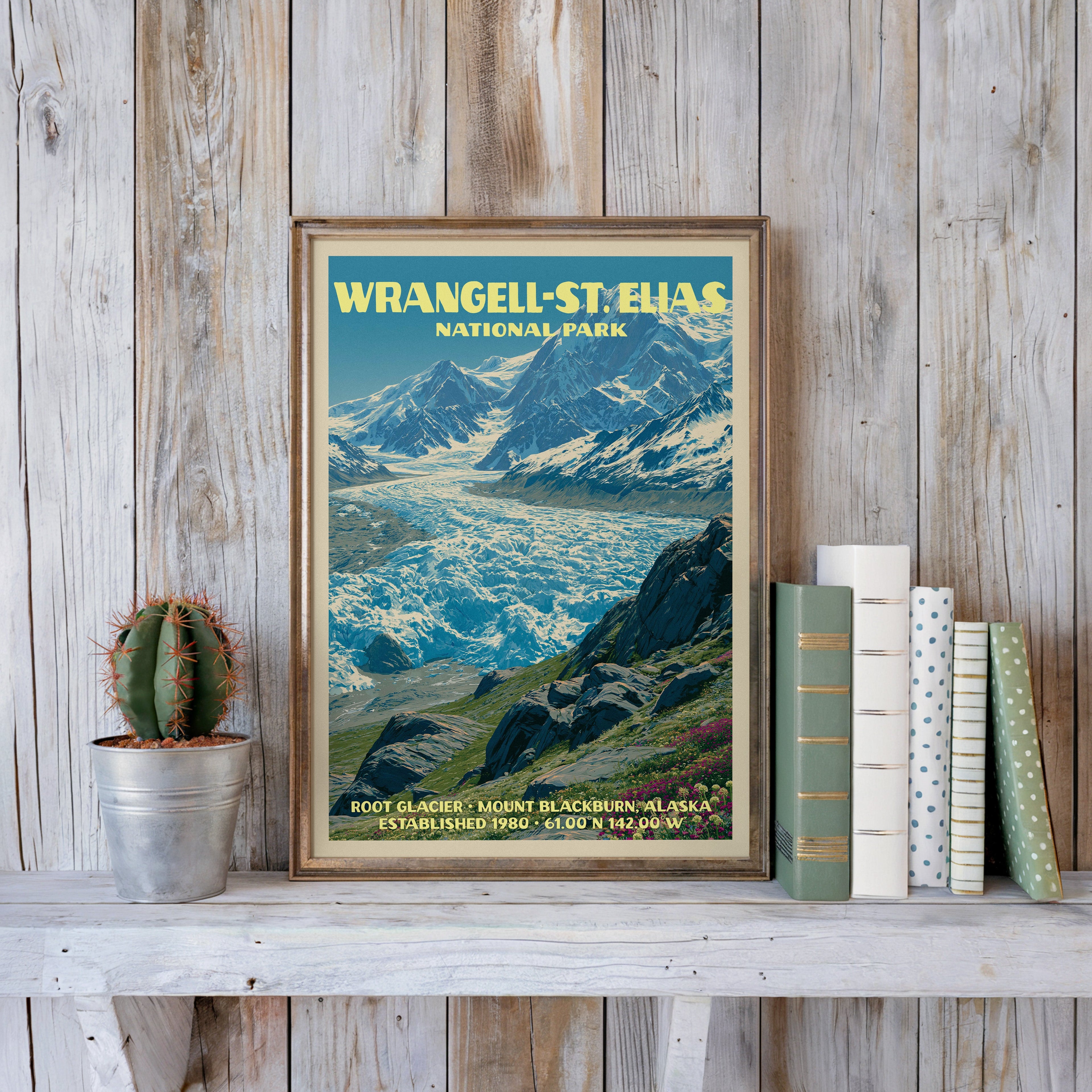 Wrangell–St. Elias vintage poster in a slim gold frame on a whitewashed plank wall beside a cactus and pastel books