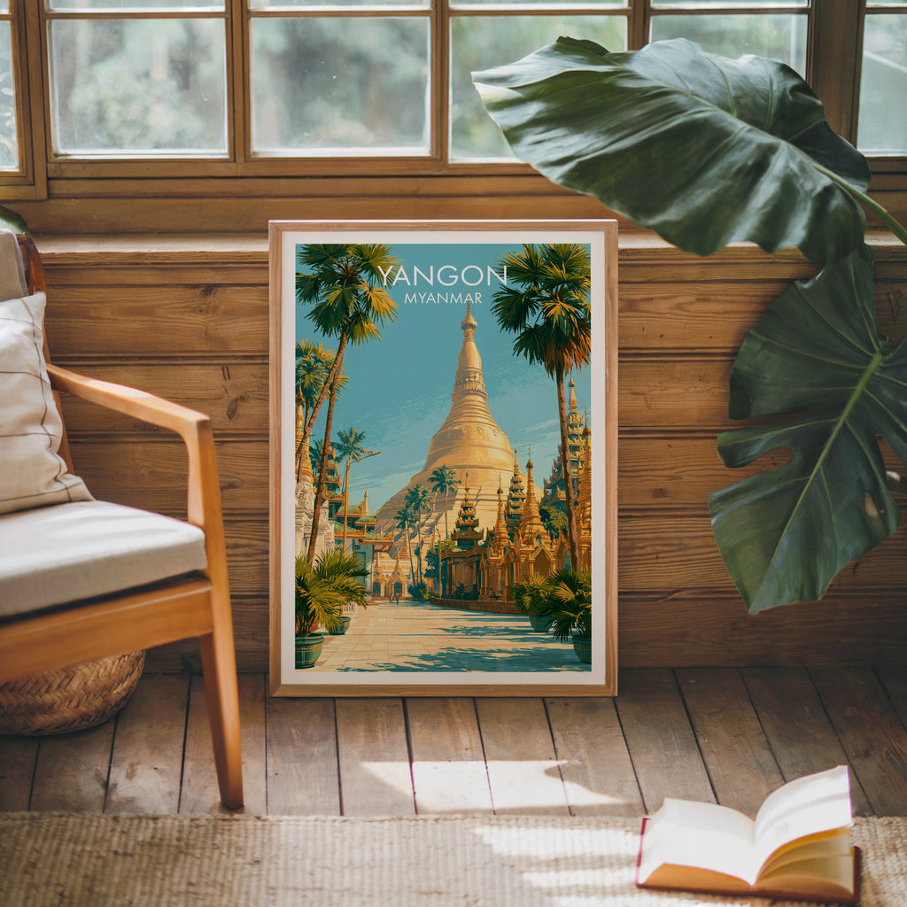 Framed Yangon Myanmar poster leaning against a timber cabin wall with monstera leaves and an open book