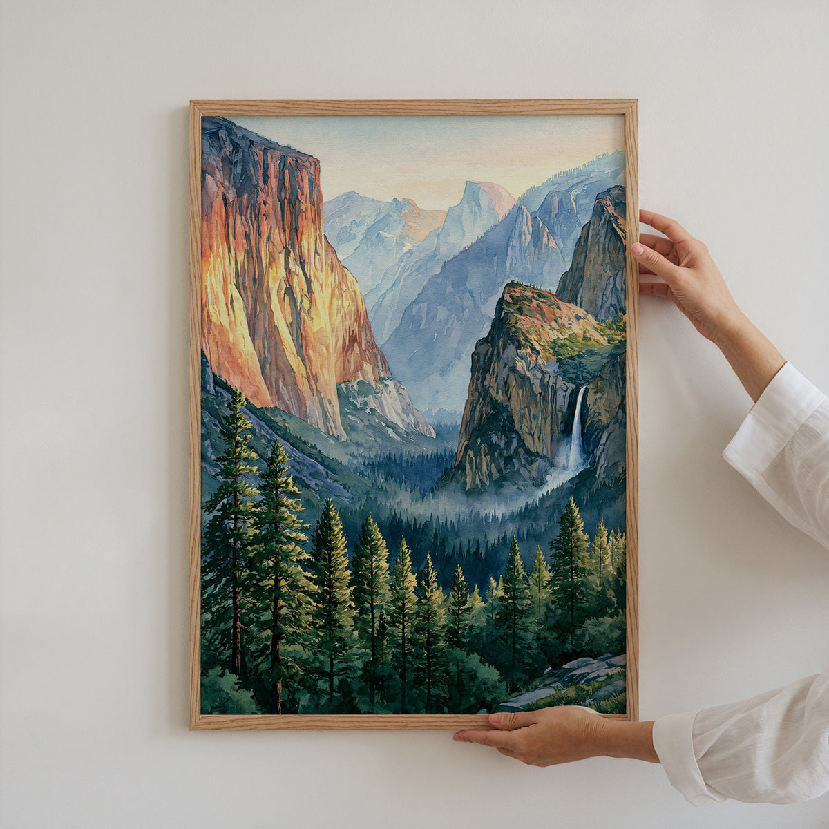 Hands holding an oak-framed Yosemite National Park watercolor art print against a plain white wall