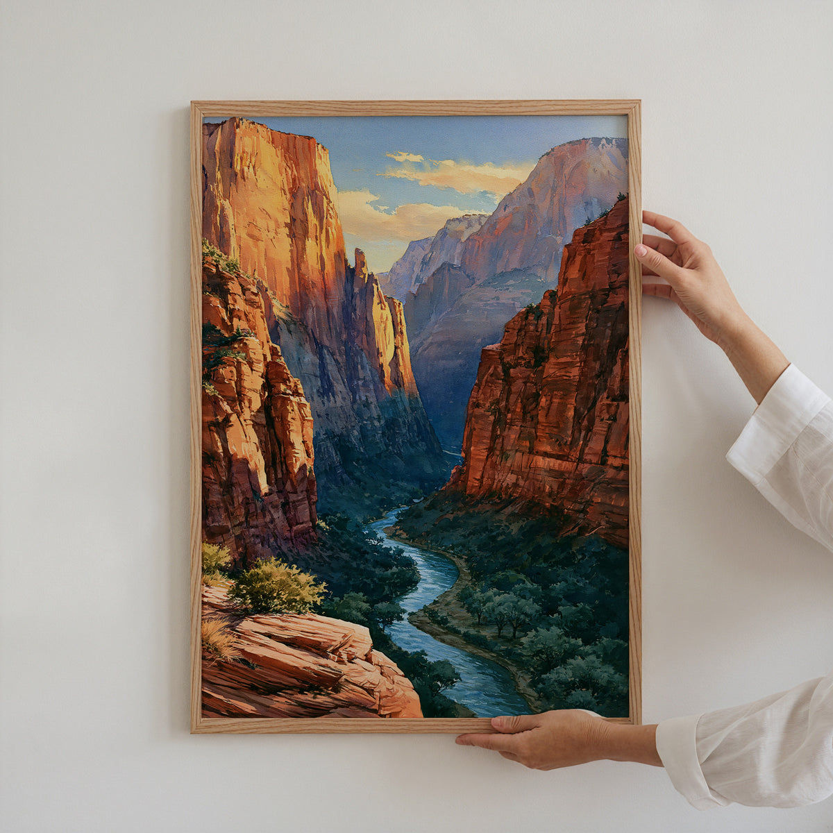 Hands holding an oak-framed Zion National Park watercolor art print against a plain white wall