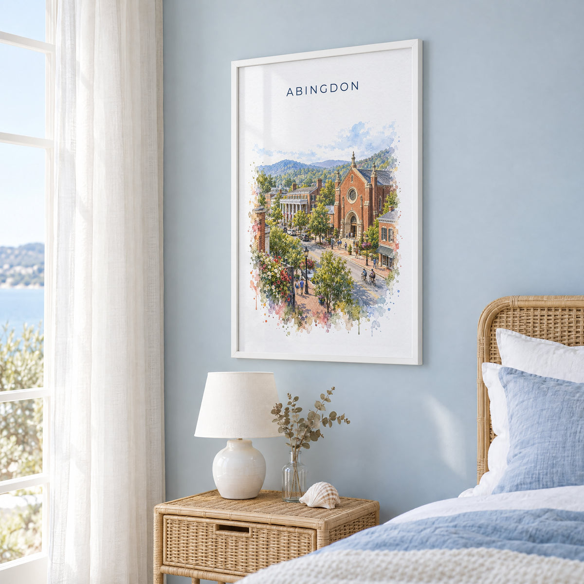Abingdon, Virginia watercolor print in a white frame on a pale blue wall beside a rattan bed in a coastal bedroom