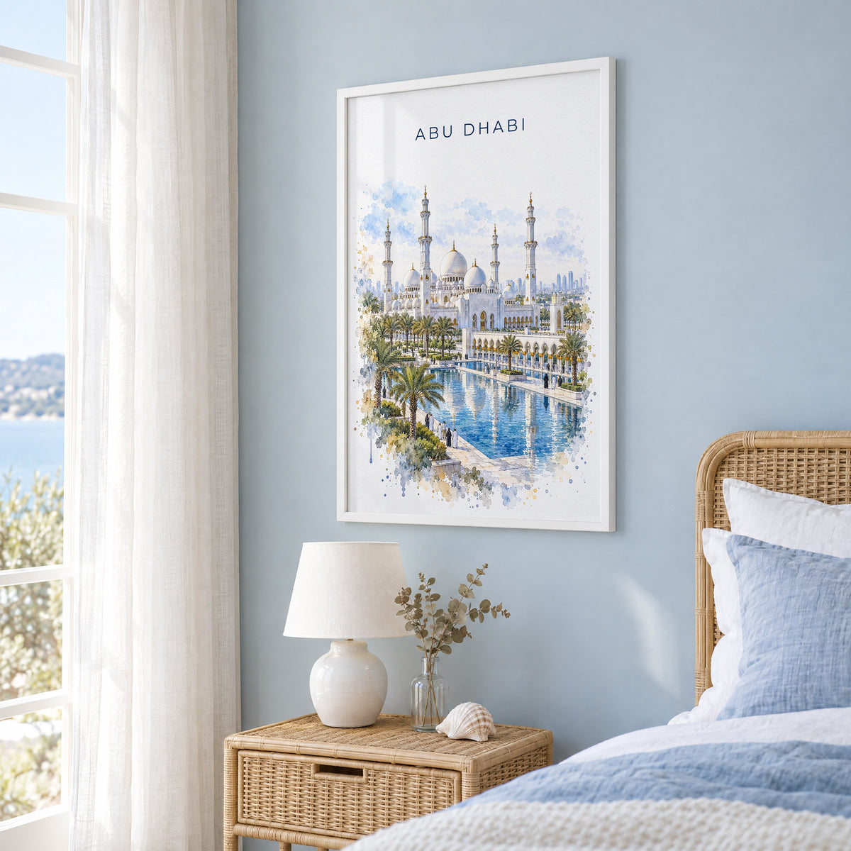Abu Dhabi watercolor print in a white frame on a pale blue wall beside a rattan bed in a coastal bedroom