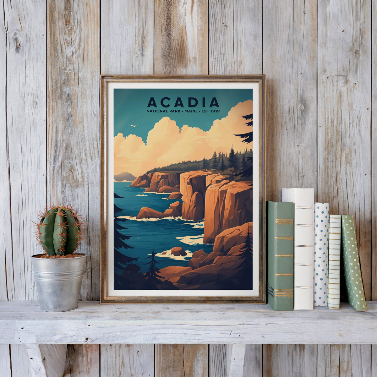 Acadia poster in an antique gold frame against whitewashed farmhouse planks beside books and a cactus