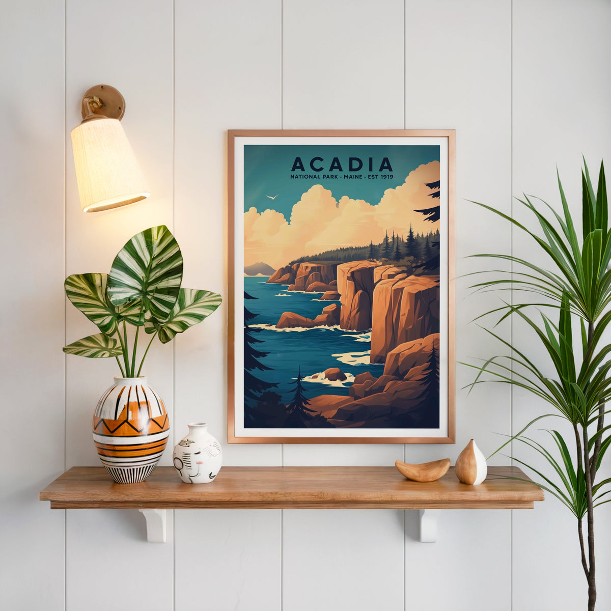 Acadia National Park print in a copper frame above an oak shelf on white shiplap with a brass sconce