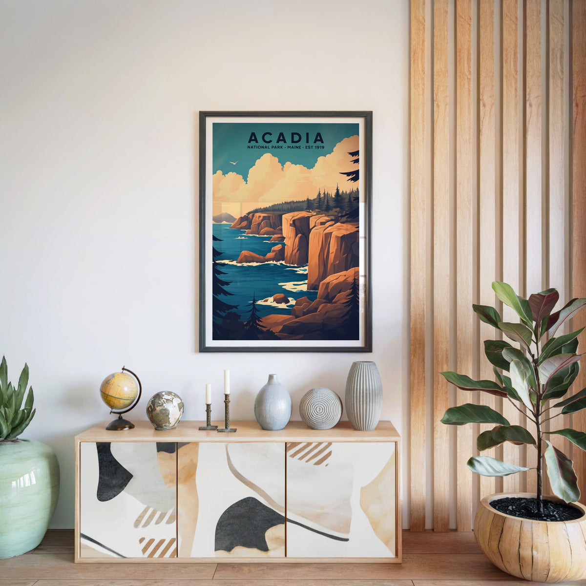 Acadia National Park print in a black frame above a light wood sideboard with a globe and ceramic vases
