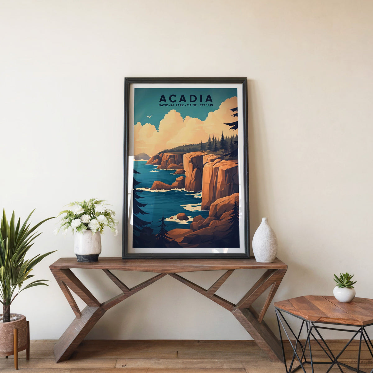 Acadia poster in a black frame on an entryway console table beside white flowers and a yucca