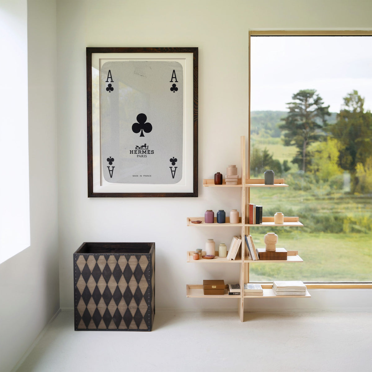 Worn vintage ace of clubs playing card print in a walnut frame with a white mat beside wooden shelves and a garden window