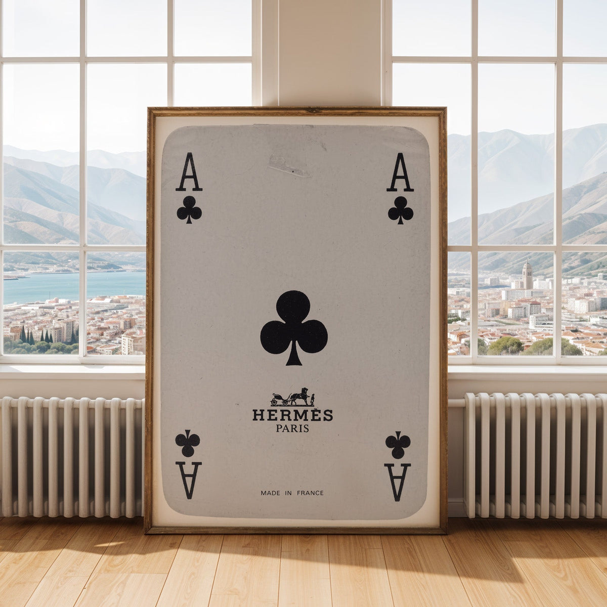 Worn vintage ace of clubs playing card print shown in an antique gold frame by tall windows with a sea view