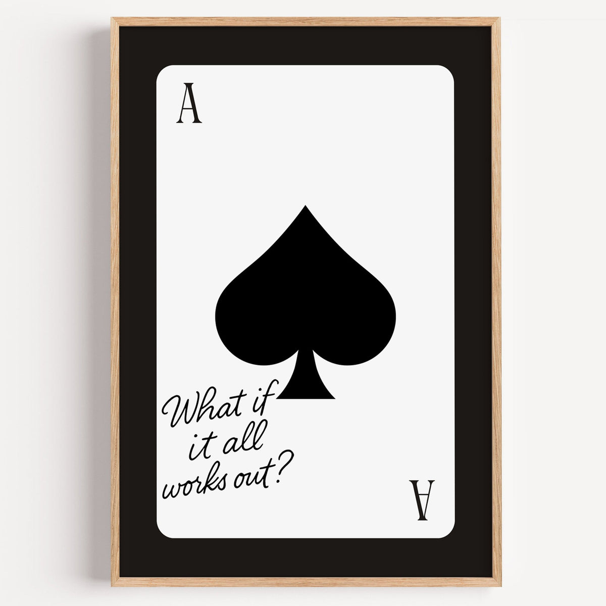Ace of spades card with What if it all works out quote print in a light oak frame on a plain white wall