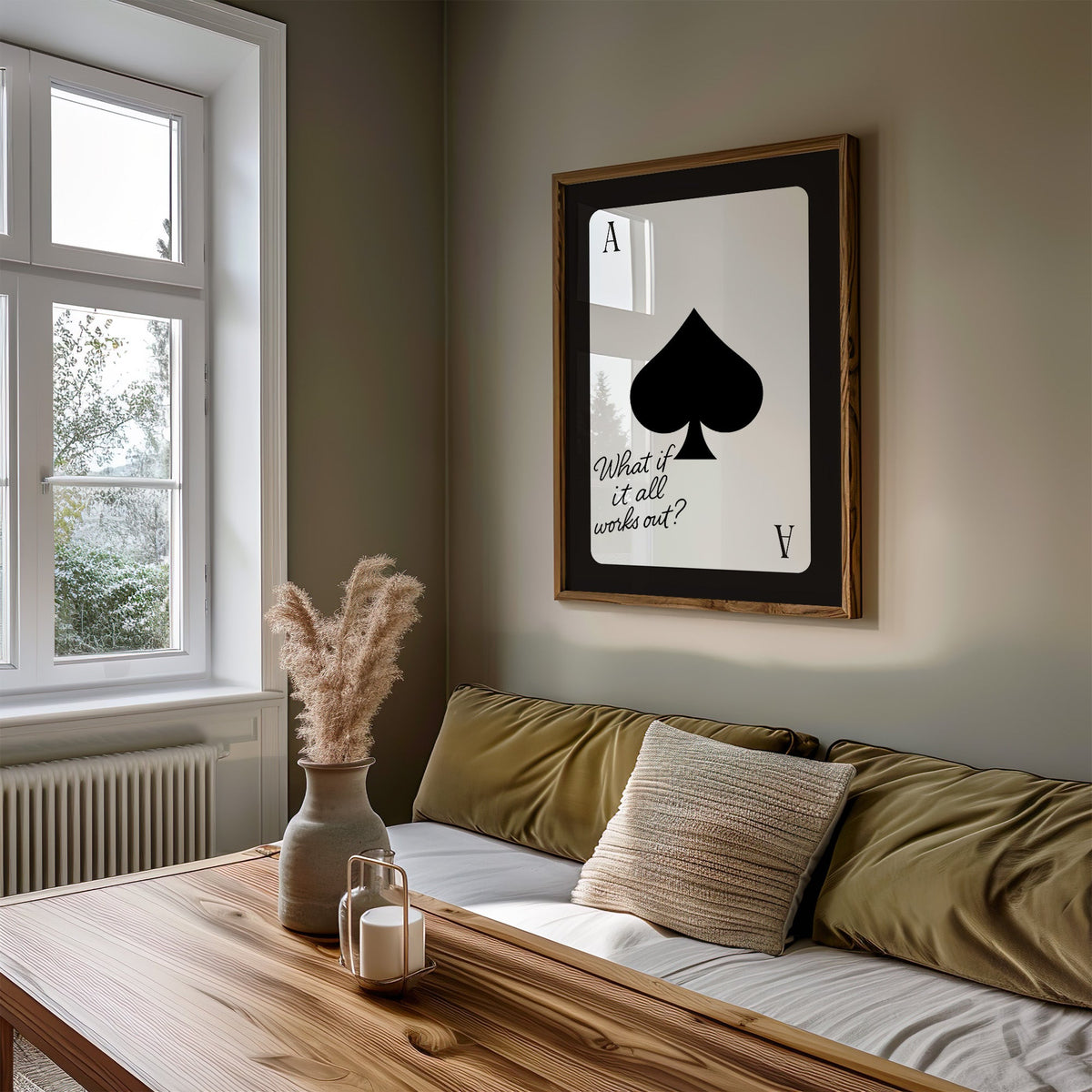 Ace of spades card with What if it all works out quote print in a walnut frame above an olive daybed by a window