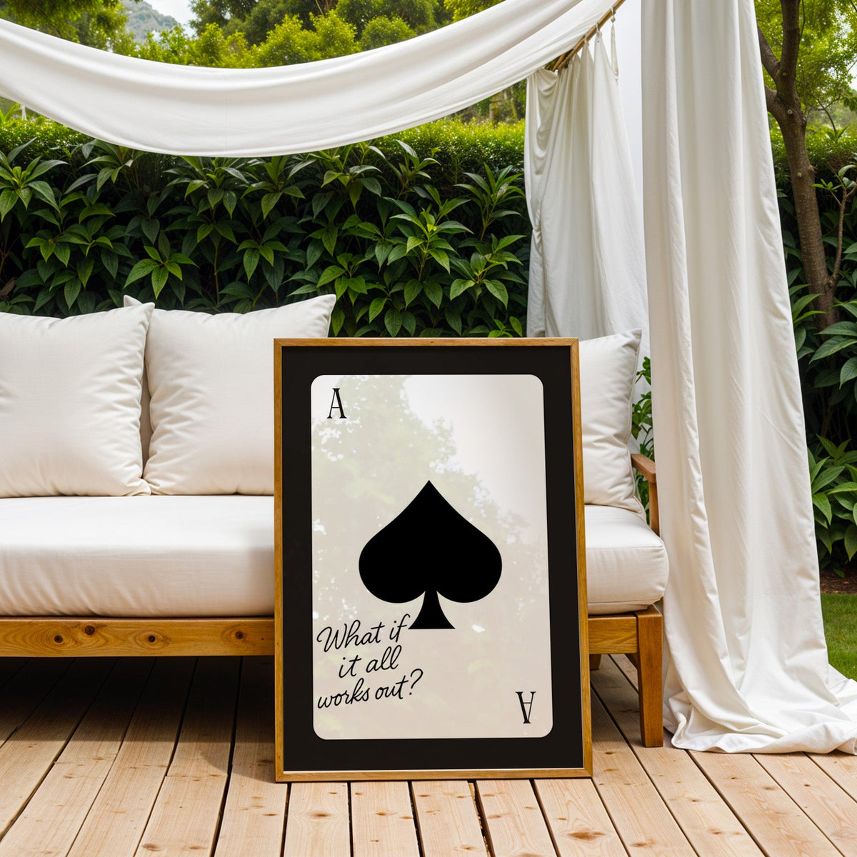 Ace of spades card with What if it all works out quote print in an oak frame on an outdoor daybed under white drapes