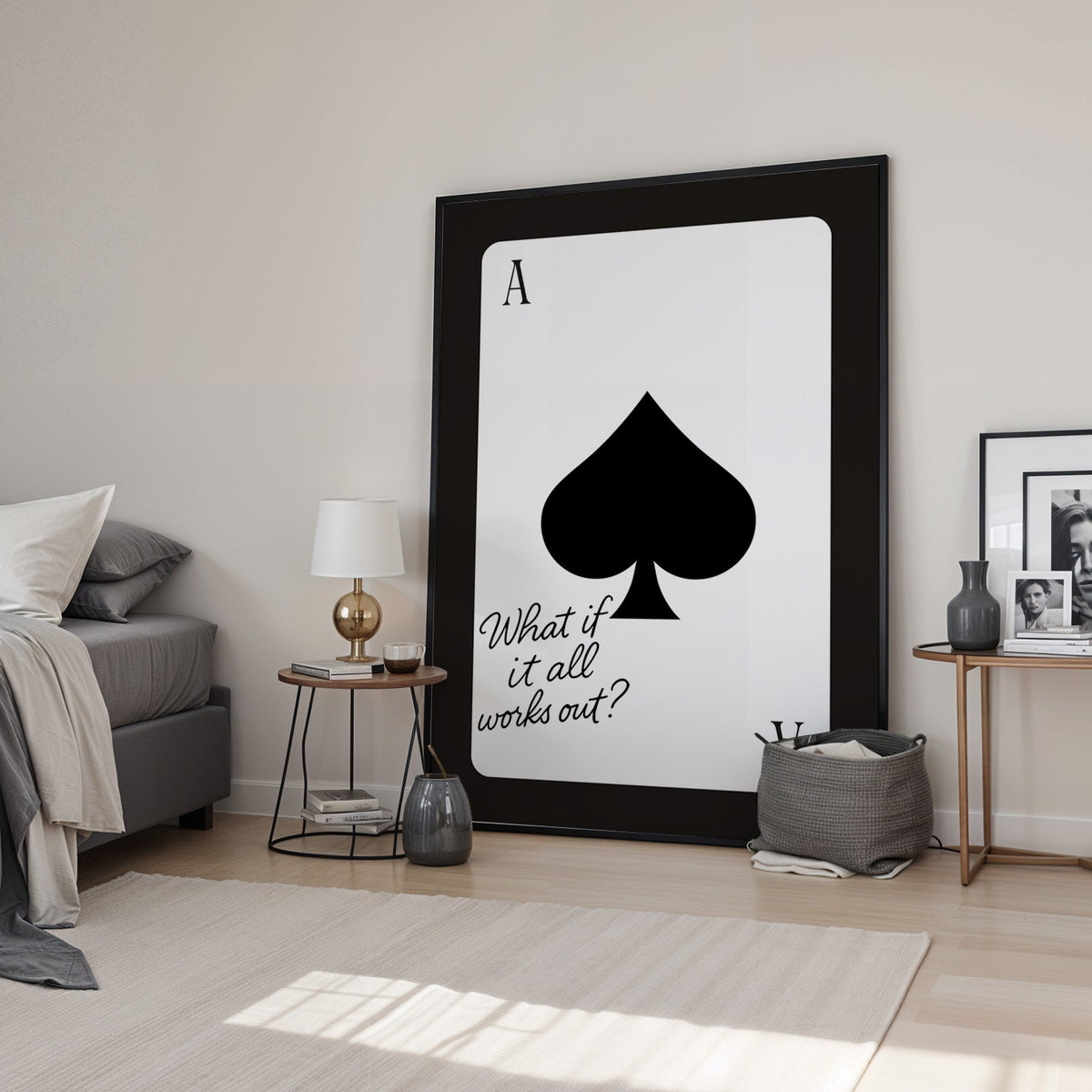 Ace of spades card with What if it all works out quote print in a black frame leaning in a bedroom beside a gold lamp