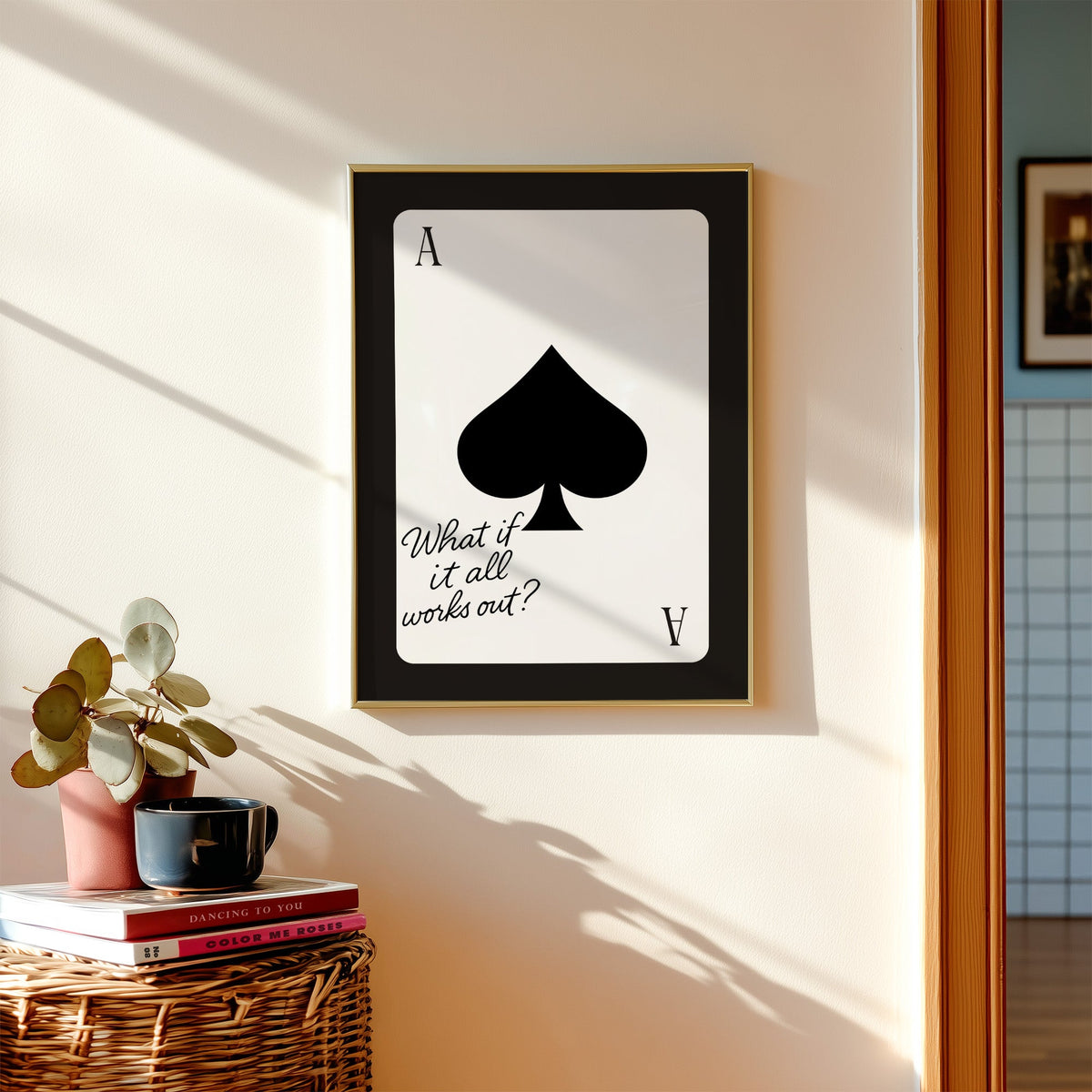 Ace of spades card with What if it all works out quote print shown in a gold frame above a wicker basket and stacked books