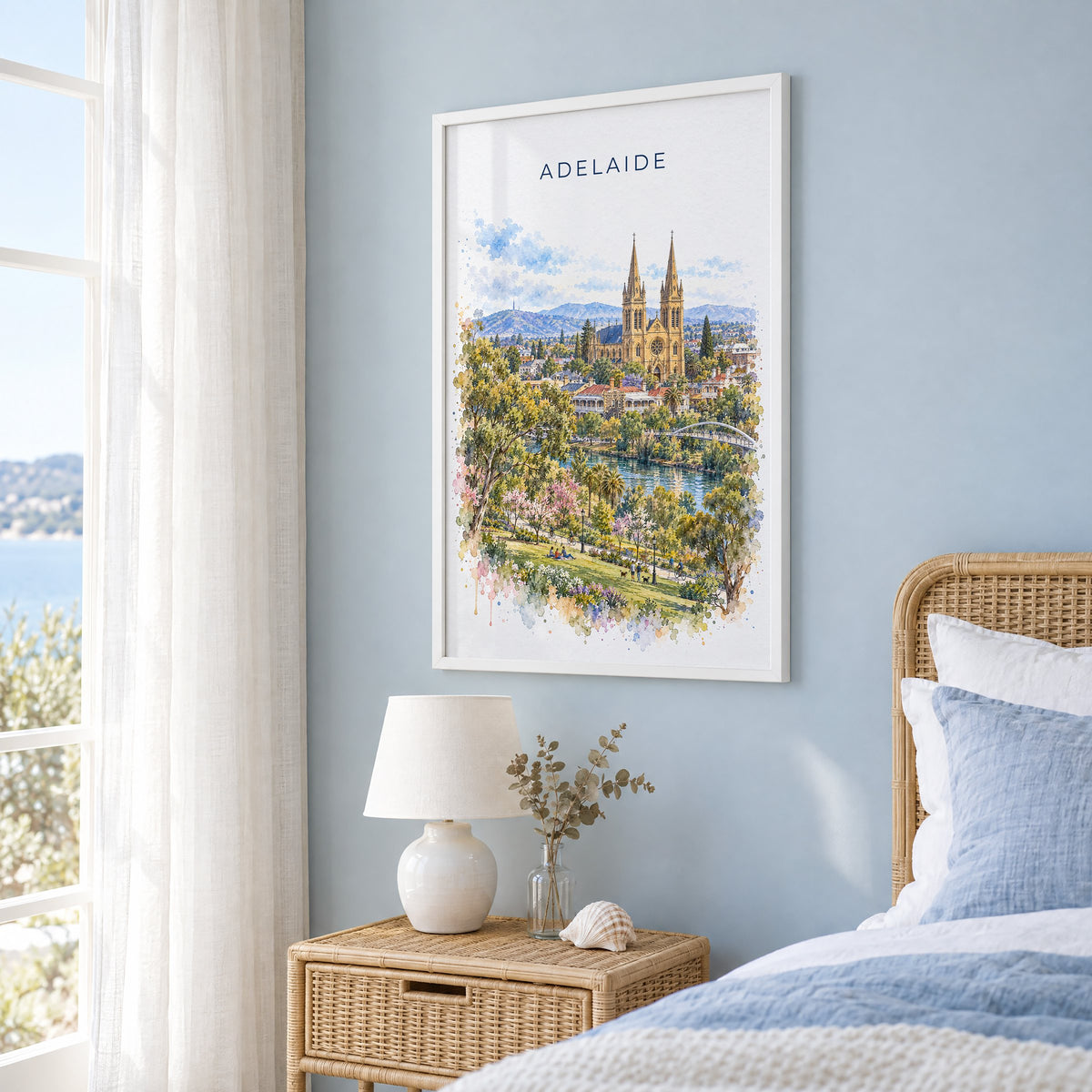 Adelaide watercolor print in a white frame on a pale blue wall beside a rattan bed in a coastal bedroom