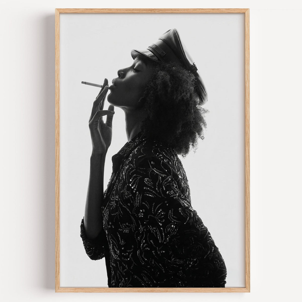 Backlit profile in leather cap with curly hair print in a light oak frame on a plain white wall