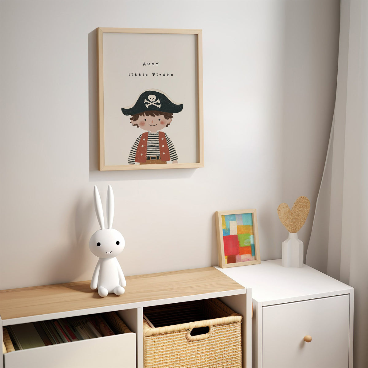 Ahoy little pirate boy nursery print in an oak frame above a kids cubby shelf with a woven basket and bunny lamp
