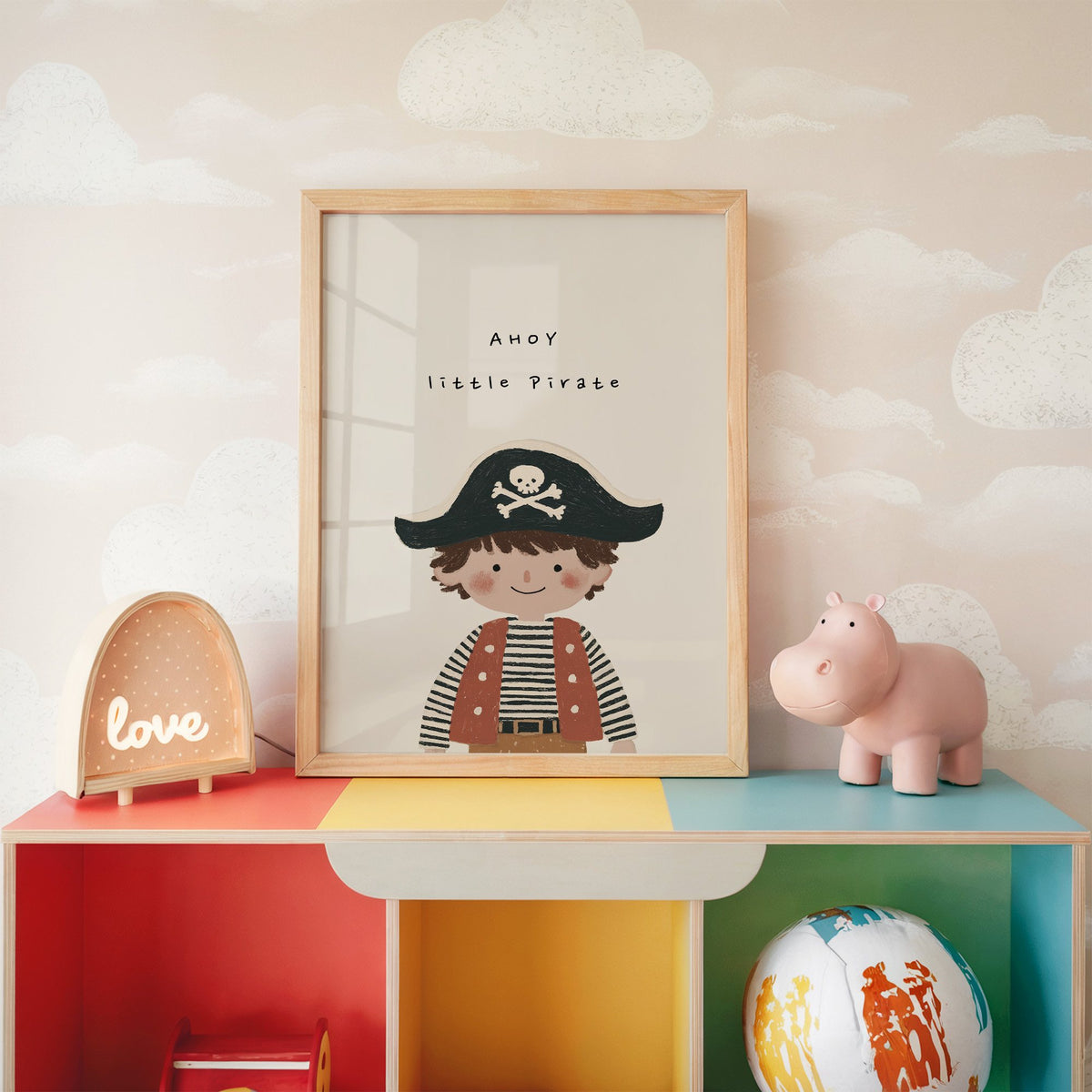 Ahoy little pirate boy nursery print in an oak frame on a rainbow toy shelf against cloud wallpaper