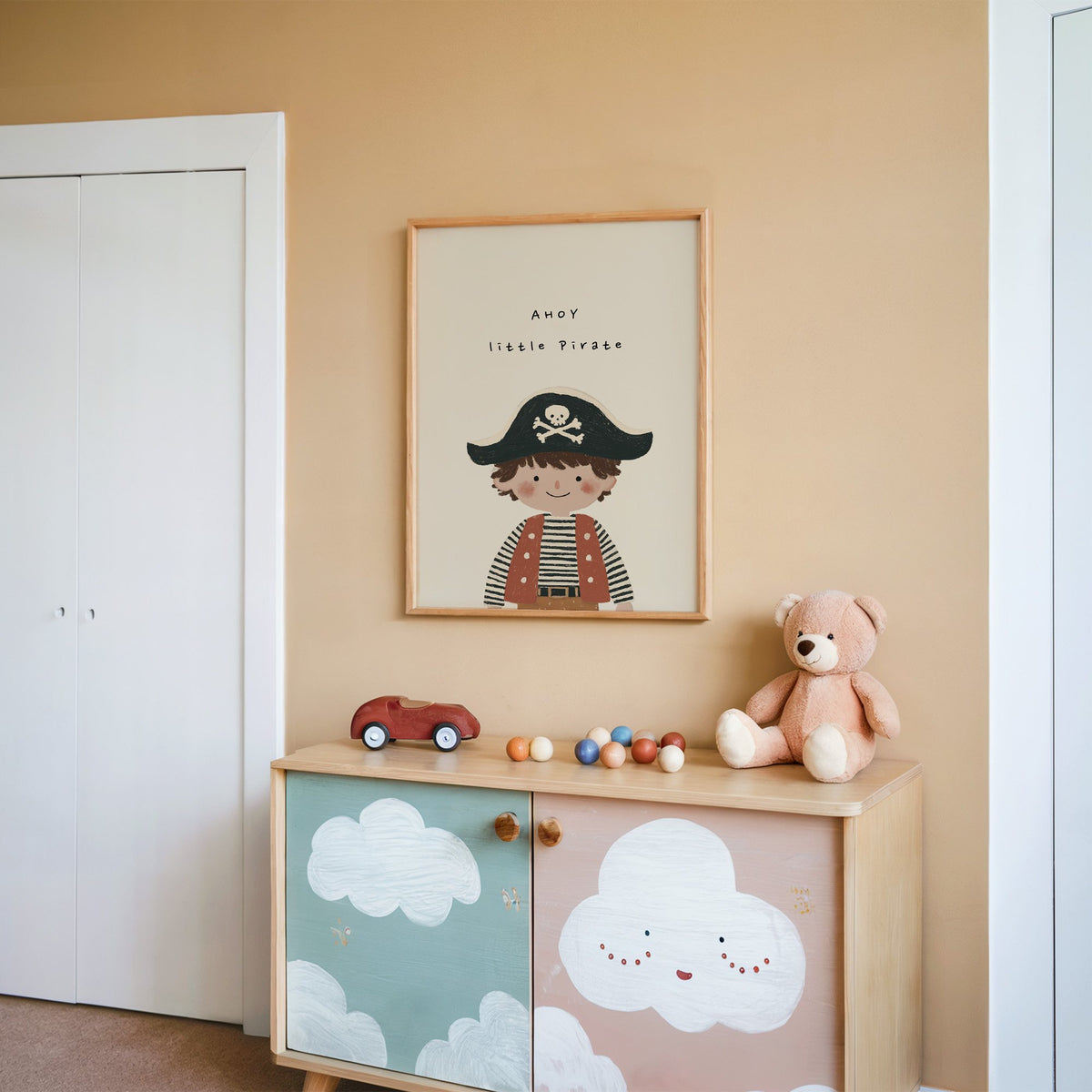 Ahoy little pirate boy nursery print in an oak frame on a peach wall above a cloud-painted cabinet