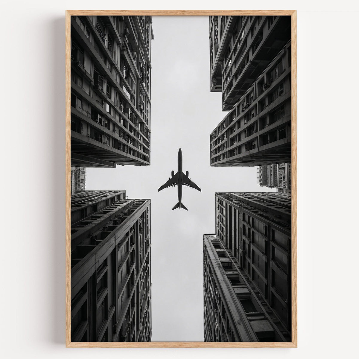Airplane flying between four skyscrapers print in a light oak frame on a plain white wall