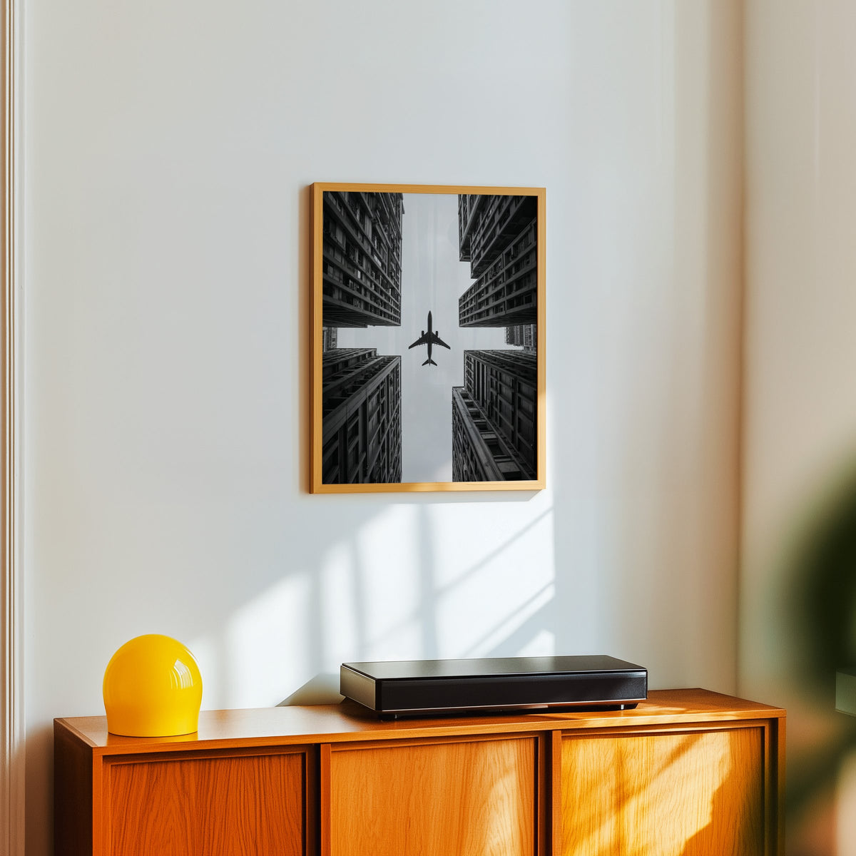 Airplane flying between four skyscrapers print in an oak frame above a teak sideboard with a yellow glass lamp