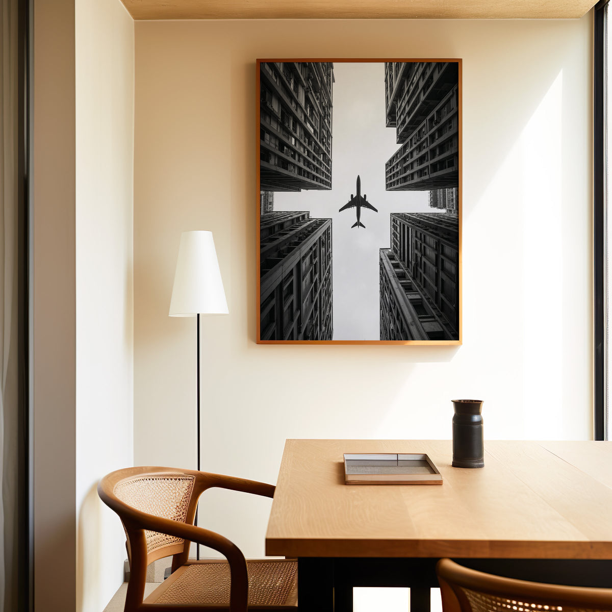 Airplane flying between four skyscrapers print in an oak frame above a dining table and cane chair