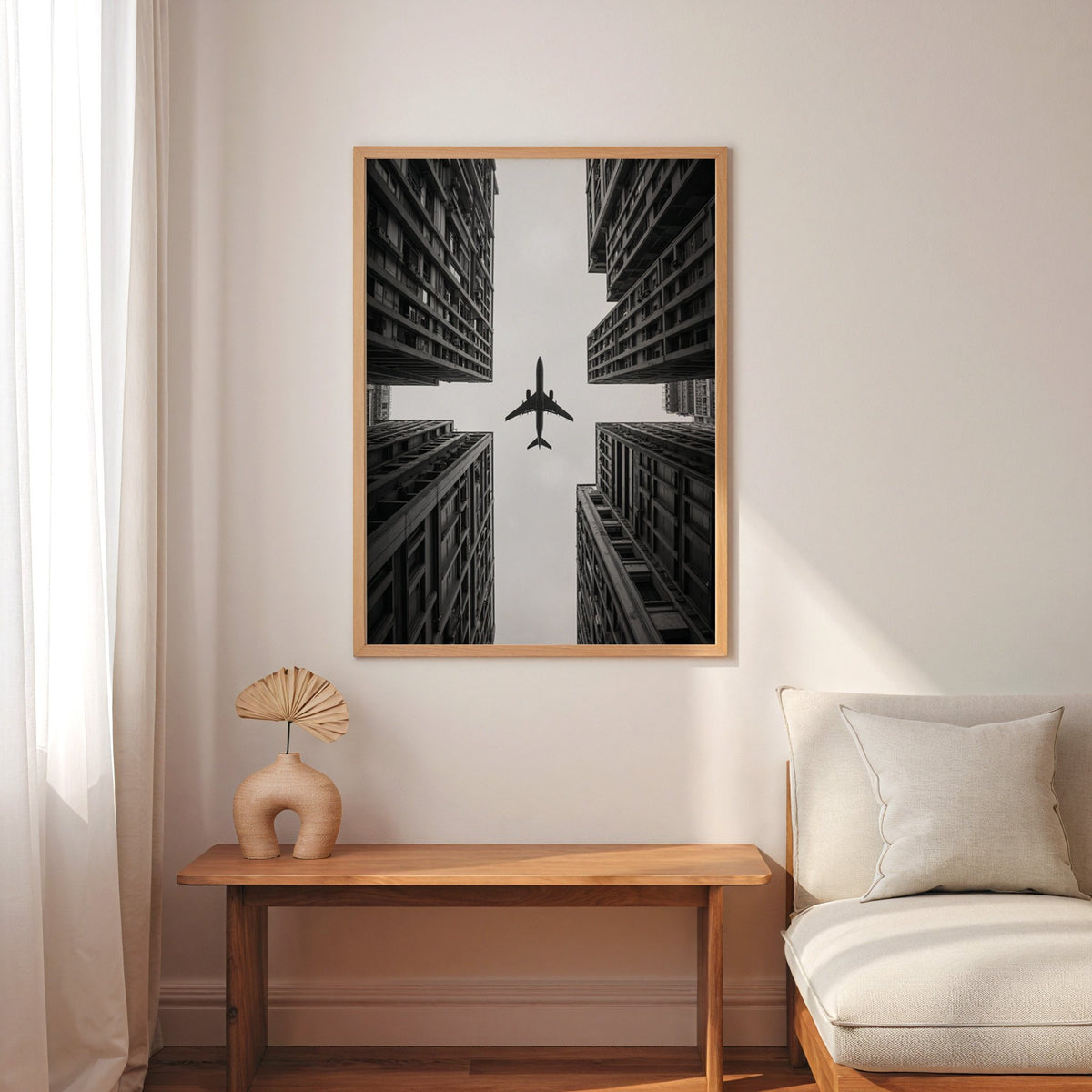 Airplane flying between four skyscrapers print in an oak frame above a narrow console with an arched vase