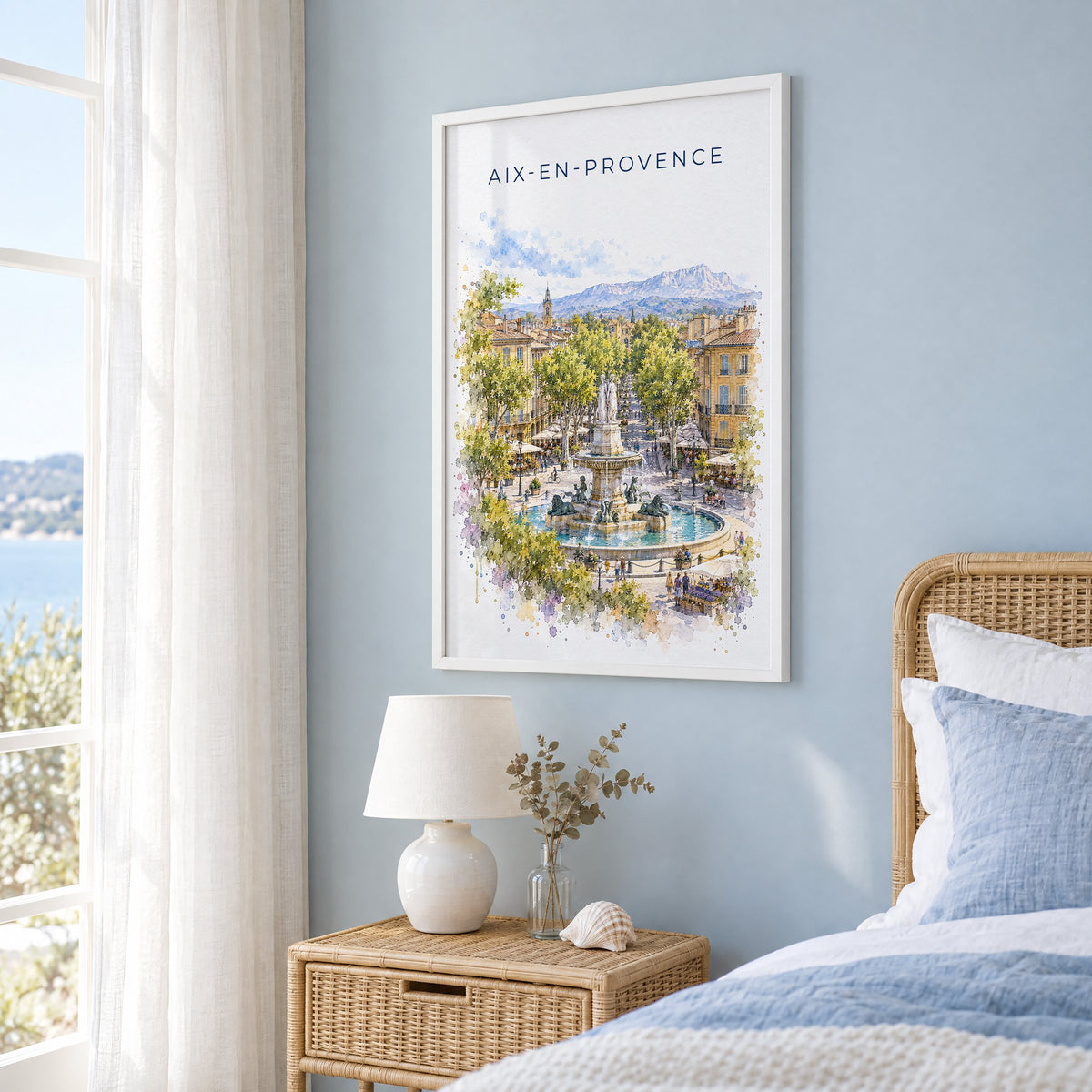 Aix-en-Provence watercolor print in a white frame on a pale blue wall beside a rattan bed in a coastal bedroom