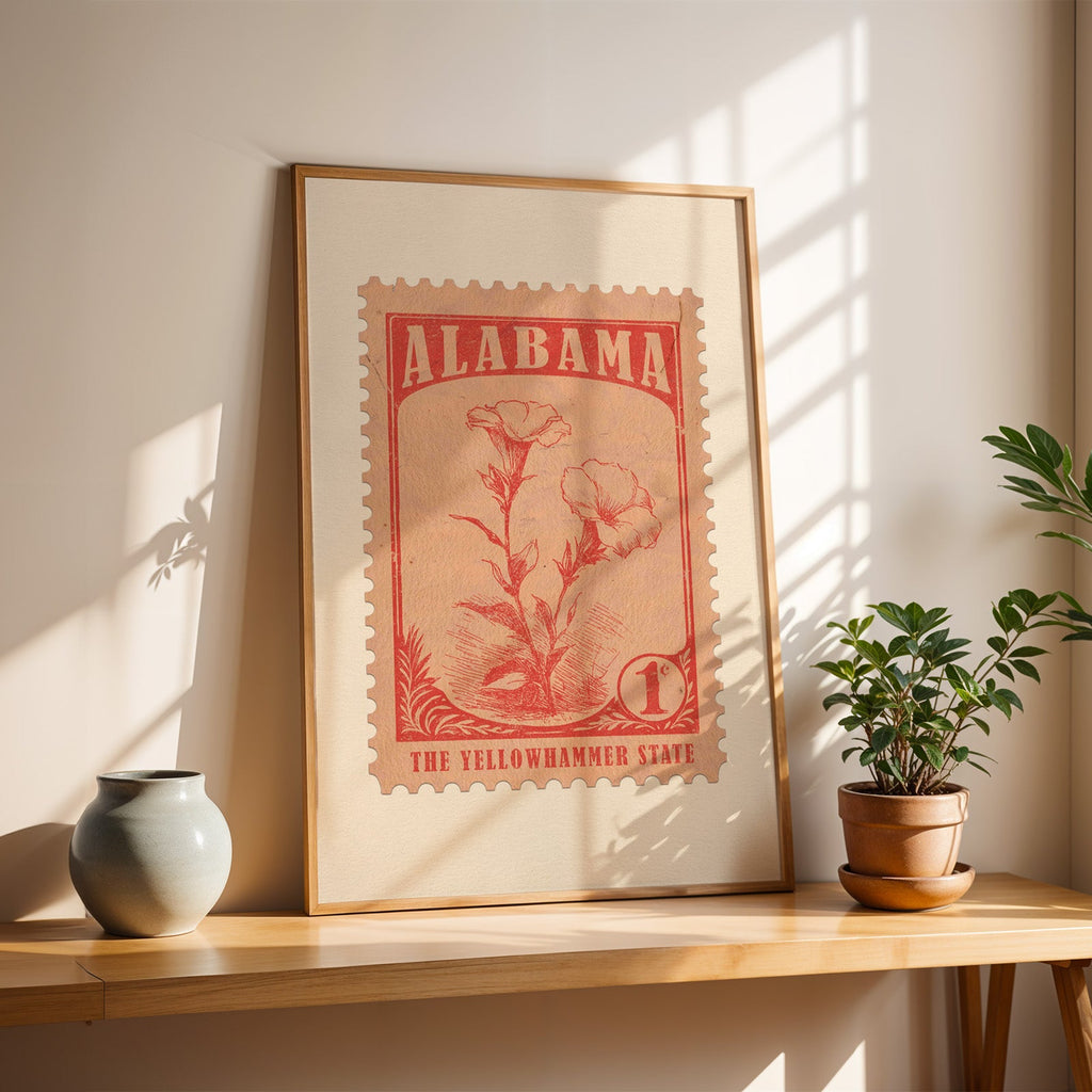 Alabama state flower stamp in a light oak frame leaning on a wooden table beside a stoneware vase and plant
