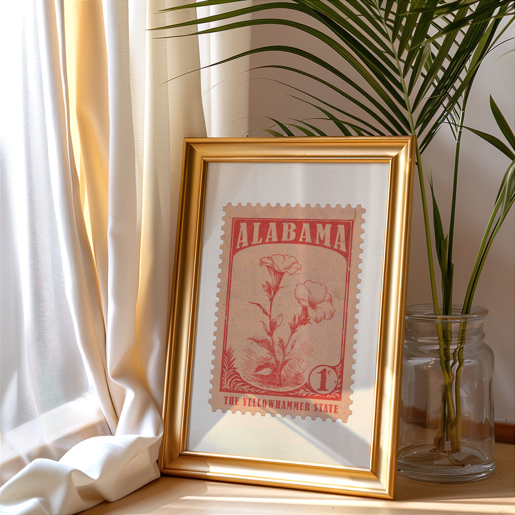 Alabama stamp print in a gold frame leaning by a cream curtain with a palm in a glass jar
