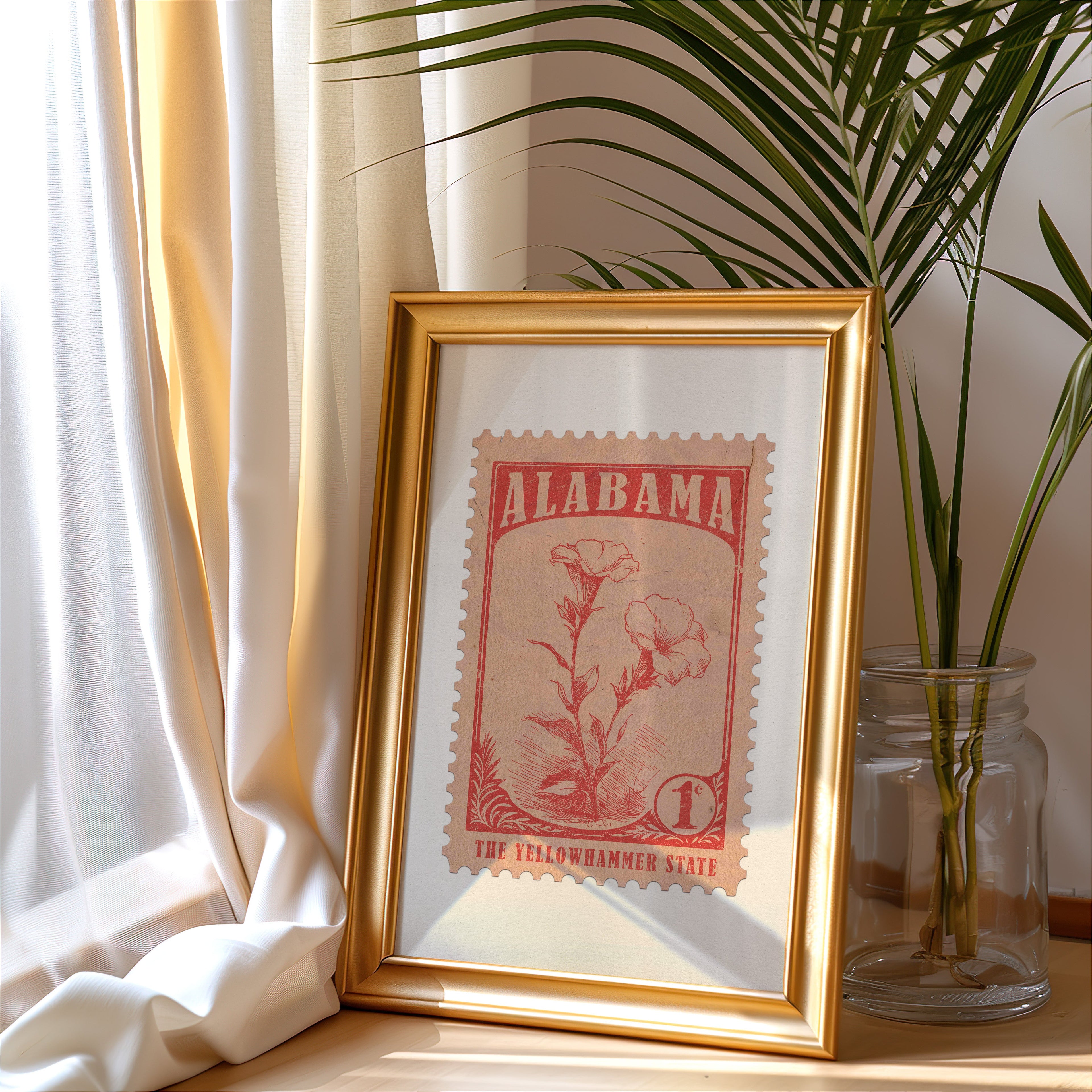 Alabama stamp print in a gold frame leaning by a cream curtain with a palm in a glass jar