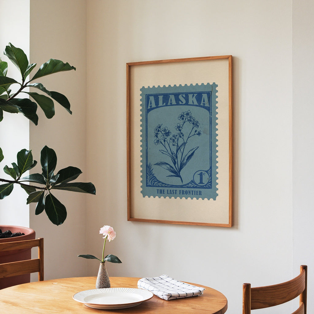Alaska state flower print framed above a round wooden table with a single bloom in a vase and books