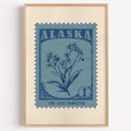 Alaska state flower stamp print in ink blue on dusty sky, light oak frame on a plain white wall
