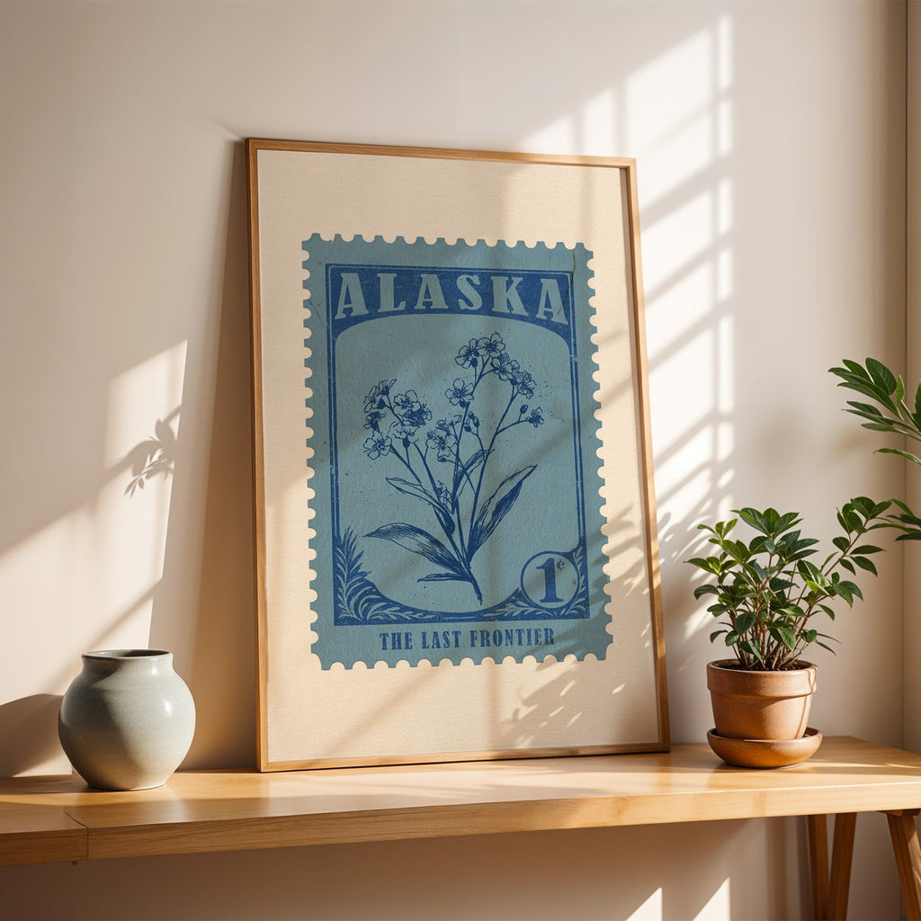 Alaska forget-me-not stamp print in a light oak frame leaning on a wooden table beside a stoneware vase