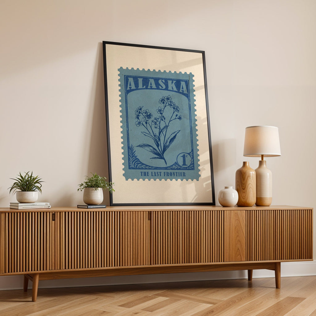 Alaska state flower print in a black frame leaning on a fluted wood credenza with vases and a table lamp