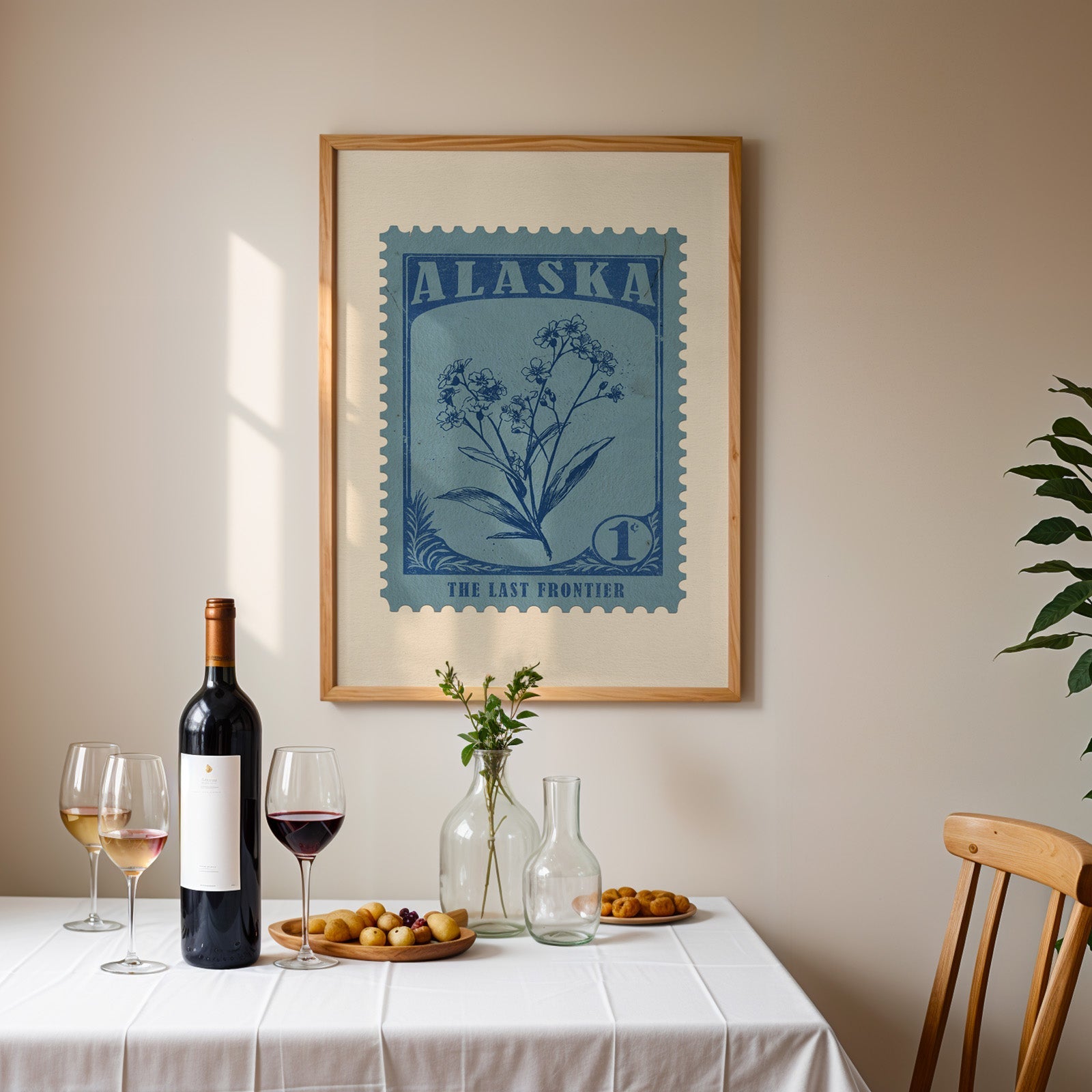 Alaska stamp print framed on the wall above a dining table set with wine, glasses and a dish of olives