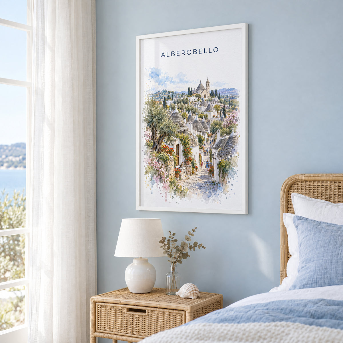 Alberobello watercolor print in a white frame on a pale blue wall beside a rattan bed in a coastal bedroom